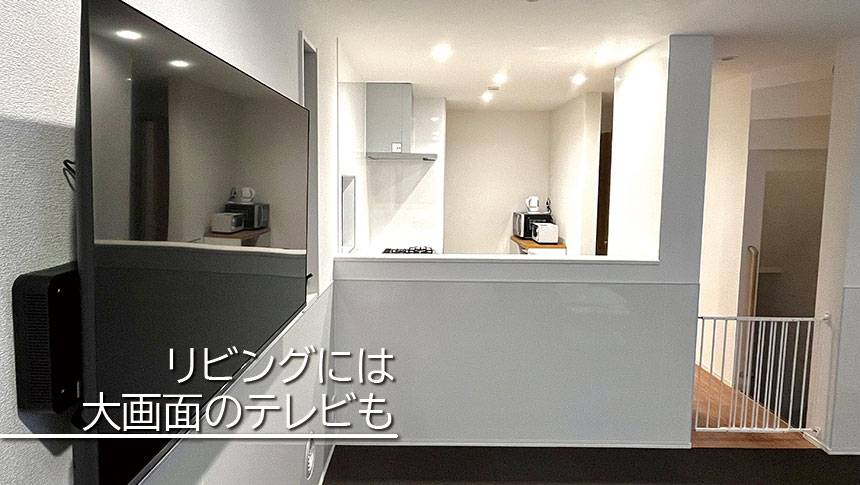 大阪・大阪ベイエリアの犬と泊まれる宿「カーサステラ10byリエゾン」｜リビングから対面キッチン方向を見たアングル。壁には大型の液晶テレビが設置されている。奥には電子レンジやケトルが見えるキッチンエリアがあり、手前には飛出し防止用の柵も設置。