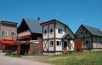 青空の下に並ぶニセコ ログ貸別荘 アルバータロッジの建物と隣接するカリー小屋