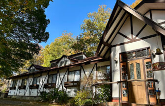 山梨県・八ヶ岳 大泉高原にあるペットと泊まれる宿『おれんじはうす』の外観。緑に囲まれた落ち着いた雰囲気のペンションと青空が広がる風景。