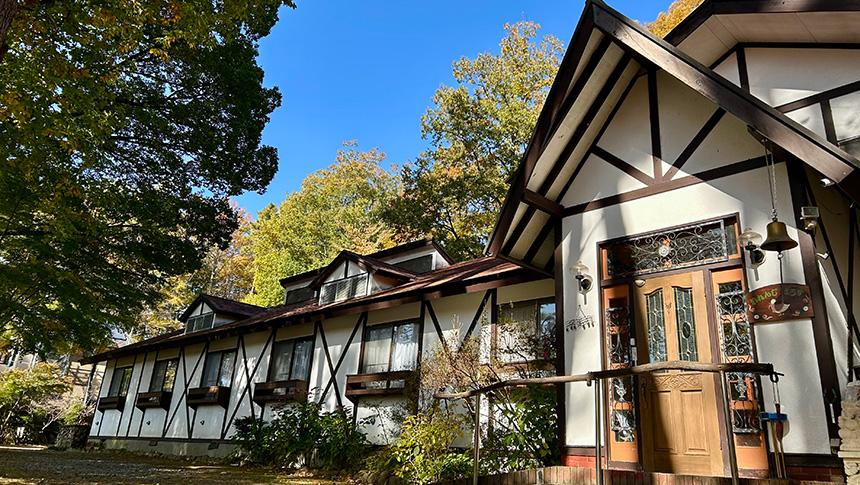 山梨県・八ヶ岳 大泉高原にあるペットと泊まれる宿『おれんじはうす』の外観。緑に囲まれた落ち着いた雰囲気のペンションと青空が広がる風景。