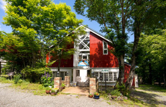 森の中に佇む、赤い外壁と大きな窓が特徴的なペンション『チップマンク』の外観