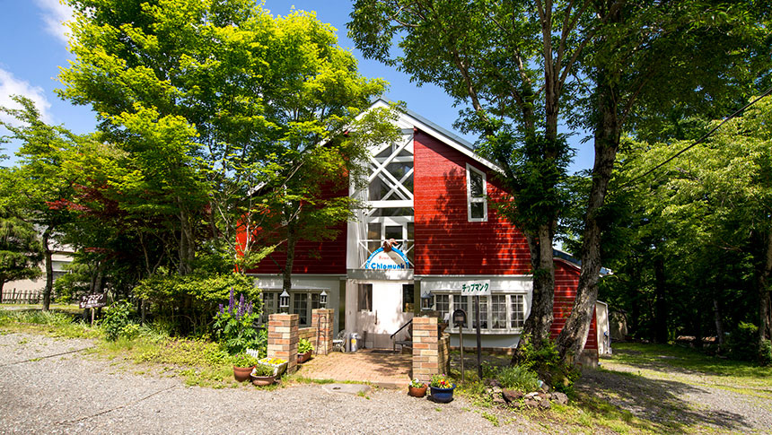 森の中に佇む、赤い外壁と大きな窓が特徴的なペンション『チップマンク』の外観
