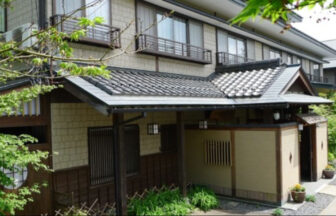 落ち着いた和モダンな趣の旅館「野辺山荘」の外観。伝統的な瓦屋根と木の質感が調和した玄関先を、新緑の葉が彩っている様子。