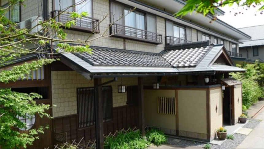 落ち着いた和モダンな趣の旅館「野辺山荘」の外観。伝統的な瓦屋根と木の質感が調和した玄関先を、新緑の葉が彩っている様子。