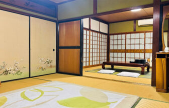 京都の里の宿「川尻」の客室。落ち着いた緑の土壁と温かみのある畳、美しい花の装飾が施された襖が特徴的な、日本の伝統的な寛ぎの空間