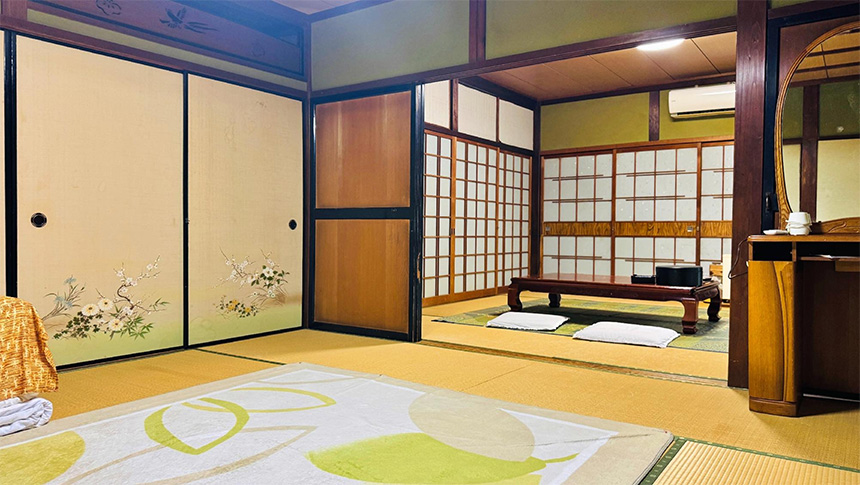 京都の里の宿「川尻」の客室。落ち着いた緑の土壁と温かみのある畳、美しい花の装飾が施された襖が特徴的な、日本の伝統的な寛ぎの空間