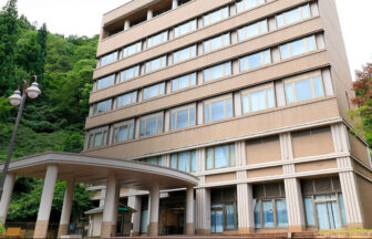 緑豊かな山を背景に建つ、越後湯沢の温泉宿「KKR湯沢ゆきぐに」の外観写真