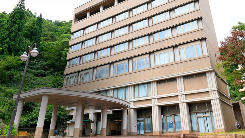 緑豊かな山を背景に建つ、越後湯沢の温泉宿「KKR湯沢ゆきぐに」の外観写真