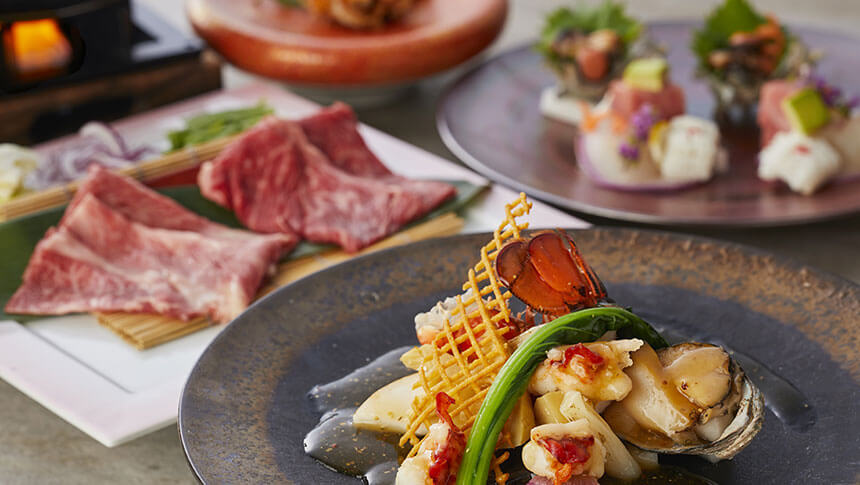 豪華な和食会席の盛り合わせ。手前にはアワビと海老の餡かけ、奥にはサシの入った厳選牛のしゃぶしゃぶ肉や新鮮なお造りが並んでいる。