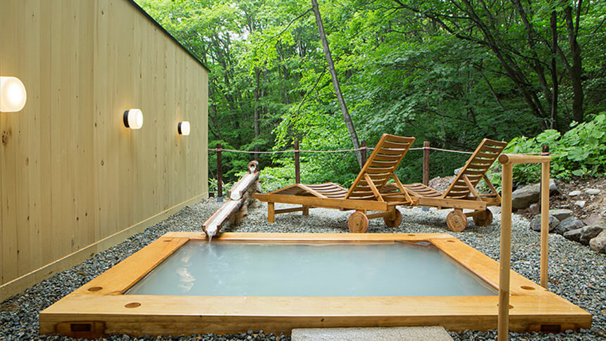 山形県・蔵王温泉にある犬と泊まれる宿「善七の湯」｜白濁したお湯（硫黄泉）が湛えられた四角い木造りの露天風呂。すぐ目の前には深い緑の森が広がり、湯上がりを涼むための木製サンラウンジャーが設置された開放的なロケーション。