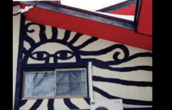 福島県裏磐梯（磐梯高原）にある「ペンション こりす」のユニークな外観。クリーム色の壁に描かれた、大きな「太陽の顔」の壁画と赤い屋根、窓。ペットと泊まれるアットホームな宿のシンボルです。