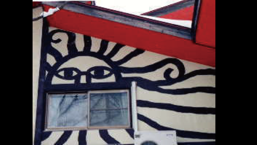 福島県裏磐梯（磐梯高原）にある「ペンション こりす」のユニークな外観。クリーム色の壁に描かれた、大きな「太陽の顔」の壁画と赤い屋根、窓。ペットと泊まれるアットホームな宿のシンボルです。