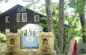 長野県・八ヶ岳中央高原　原村の犬と泊まれる宿「Wandsworth」｜石造りの門柱と『Wandsworth』の看板が印象的な、木々に囲まれた英国風コテージの外観。黒い木壁に白い窓枠が映えるシックな建物