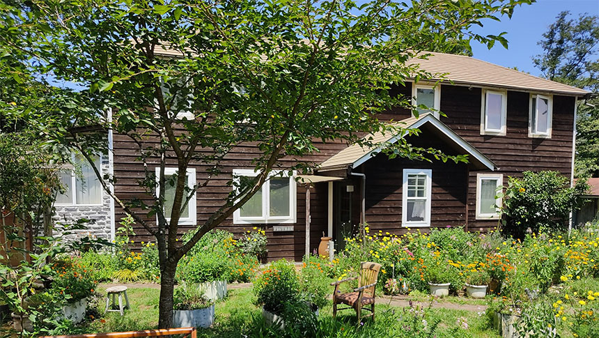 静岡県・伊豆高原の犬と泊まれる宿「ペンションfigtree（フィグツリー）」｜色とりどりの花々が咲き誇る豊かな庭と、その奥に佇む白い窓枠が特徴的な2階建ての木造ログハウス