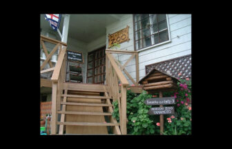 兵庫県淡路市にある犬と泊まれる宿「ペンションZOO」のエントランス。木製の階段の先にアットホームな玄関があり、看板には「PENSION ZOO」の文字。階段横には花々が咲き、ログハウス風のポストが置かれた温かみのある外観