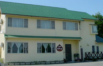 滋賀県・マキノにある犬と泊まれる宿「ペンション くりっこ」の外観。明るいクリーム色の外壁にグリーンの屋根が映える、アットホームな雰囲気の2階建てペンション