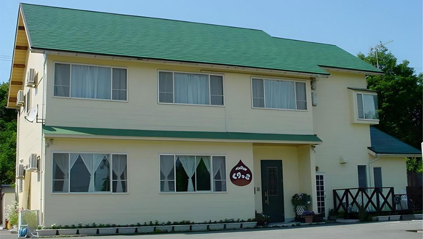 滋賀県・マキノにある犬と泊まれる宿「ペンション くりっこ」の外観。明るいクリーム色の外壁にグリーンの屋根が映える、アットホームな雰囲気の2階建てペンション