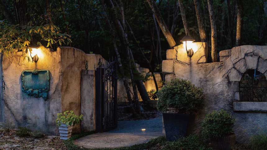 滋賀県大津市北比良にある「オーベルジュ メソン」の夜のエントランス。暖かなアンティークライトに照らされた石造りの壁と、緑色のレリーフ看板、鉄製の門が静かな森の中に佇む様子。1日4組限定の隠れ家宿。