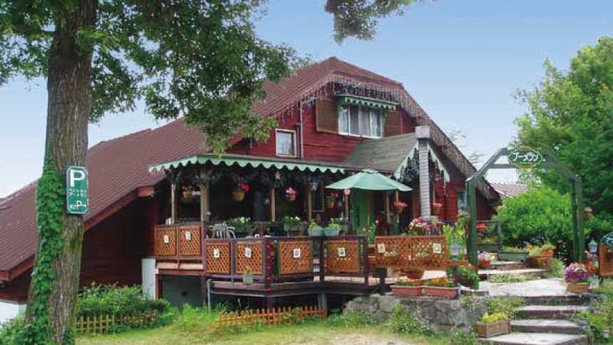 鳥取県大山にあるペットと泊まれる宿『ペンションブーメラン』の赤い木造の外観と、花に囲まれた開放的なウッドデッキテラス