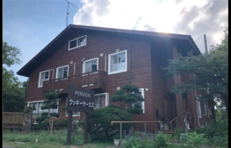 鳥取県・大山のペンション　クッキーサーカス｜緑豊かな木々に囲まれた、落ち着いた茶色の木造2階建てペンション。入り口に立つ手作り感のある看板が目印