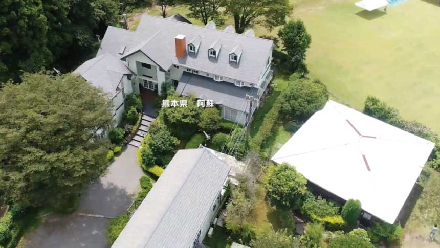 ペンションベルバードの全景空撮。豊かな森に囲まれた白い洋館と広大な芝生広場