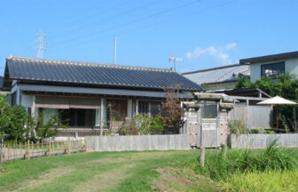 鹿児島県｜青空の下に建つ、黒瓦屋根が特徴的な平屋造りの「いやしの宿 いにしえ」の外観と芝生の庭