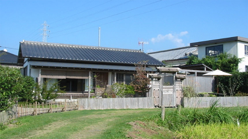 鹿児島県｜青空の下に建つ、黒瓦屋根が特徴的な平屋造りの「いやしの宿 いにしえ」の外観と芝生の庭