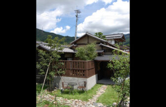 青空と山々を背景にした、福岡県の犬と泊まれる秋月古民家貸別荘「我道庵」の外観。芝生の庭にはテラス席があり、伝統的な平屋建築の落ち着いた佇まい。