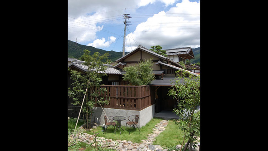 青空と山々を背景にした、福岡県の犬と泊まれる秋月古民家貸別荘「我道庵」の外観。芝生の庭にはテラス席があり、伝統的な平屋建築の落ち着いた佇まい。