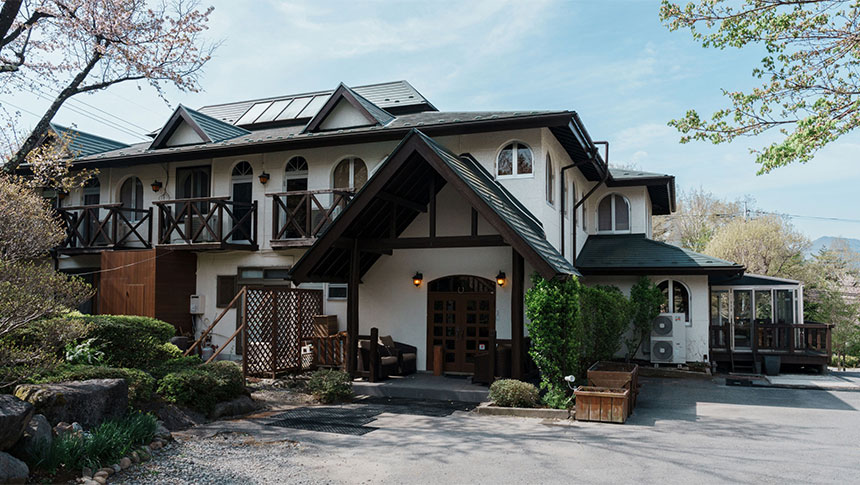 山梨県・小淵沢にある「ロッジ・アトリエ」の外観。三角屋根のエントランスと白い壁が特徴的な洋風の建物