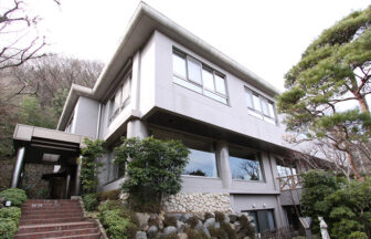 神奈川県にある犬と泊まれる宿「土ぐレストプレイス」｜和モダンな外観。左側には入り口へ続くレンガ風の階段があり、右側には立派な松の木が植えられています。背後には緑豊かな山が迫り、自然に囲まれた静かな佇まいです