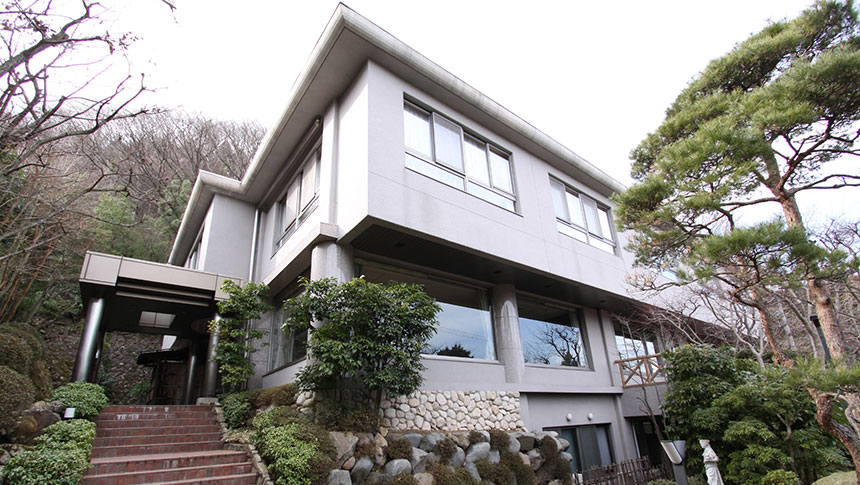 神奈川県にある犬と泊まれる宿「土ぐレストプレイス」｜和モダンな外観。左側には入り口へ続くレンガ風の階段があり、右側には立派な松の木が植えられています。背後には緑豊かな山が迫り、自然に囲まれた静かな佇まいです