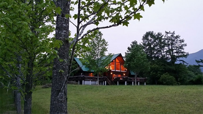 岡山県・蒜山のNadja ゲストハウス｜森と草原に囲まれた静かなログハウス。夕闇の中で室内から漏れる温かな光が印象的なコテージの風景