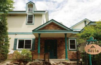 栃木県那須町にある「Hotel Resta（ホテルレスタ）」のレンガ調の玄関外観。緑色の柱と、丸い施設看板が立っている。