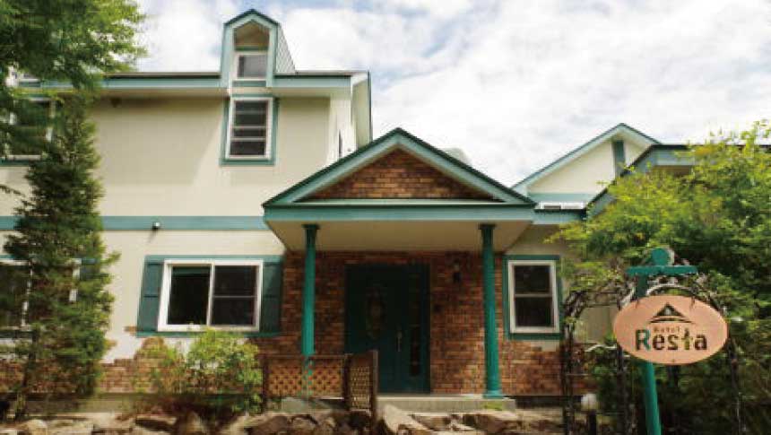 栃木県那須町にある「Hotel Resta（ホテルレスタ）」のレンガ調の玄関外観。緑色の柱と、丸い施設看板が立っている。