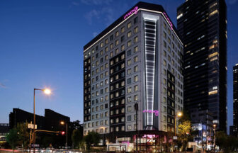 大阪・梅田の犬と泊まれる宿「モクシー大阪新梅田」｜夜空を背景に、ピンクのネオンロゴが輝くスタイリッシュな高層ホテルの外観。都会的でモダンな建築デザインが特徴