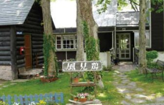 新潟県妙高高原にある宿「ウッディハウス風見鶏」の、緑豊かな庭とログハウス風の建物外観