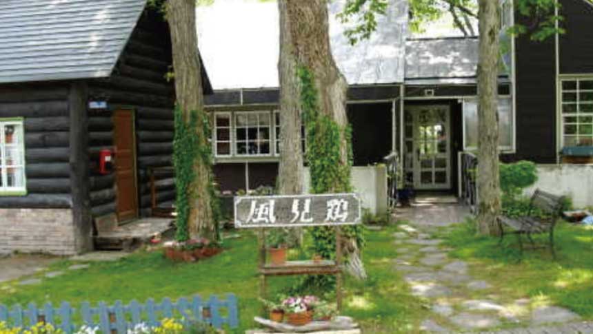 新潟県妙高高原にある宿「ウッディハウス風見鶏」の、緑豊かな庭とログハウス風の建物外観