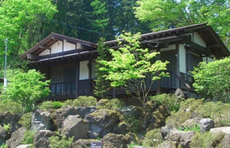 山梨県の愛犬と泊まれる「やすらぎの別邸 四季亭」｜緑豊かな山林を背に、大きな岩が配置された斜面に建つ「やすらぎの別邸 四季亭」の和風コテージの外観。新緑の木々に囲まれた落ち着いた佇まい。