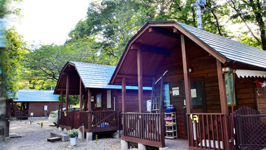 那須高原にある「cottage WANS（コテージわん’S）」の木造コテージの外観。緑豊かな自然の中に青い屋根のログハウスが並ぶ様子。
