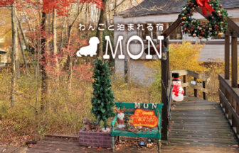 紅葉の森の中に佇む「わんこと泊まれる宿 MON」のペンション建物の外観。アプローチにはロゴが彫られた常設の木の看板が立っている。