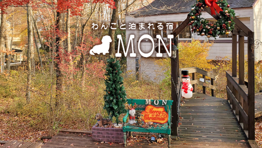 紅葉の森の中に佇む「わんこと泊まれる宿 MON」のペンション建物の外観。アプローチにはロゴが彫られた常設の木の看板が立っている。