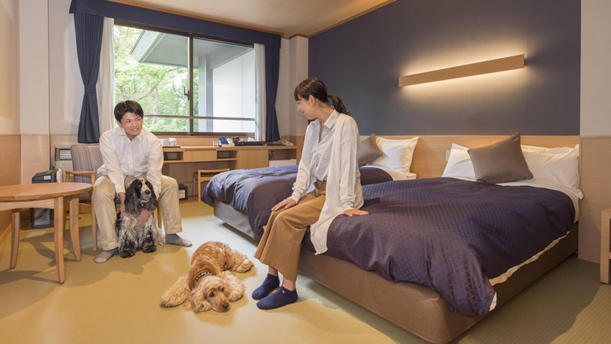 わんわんパラダイス プレミア山中湖の和洋室客室。ベッドとリビングスペースで愛犬と過ごす様子。