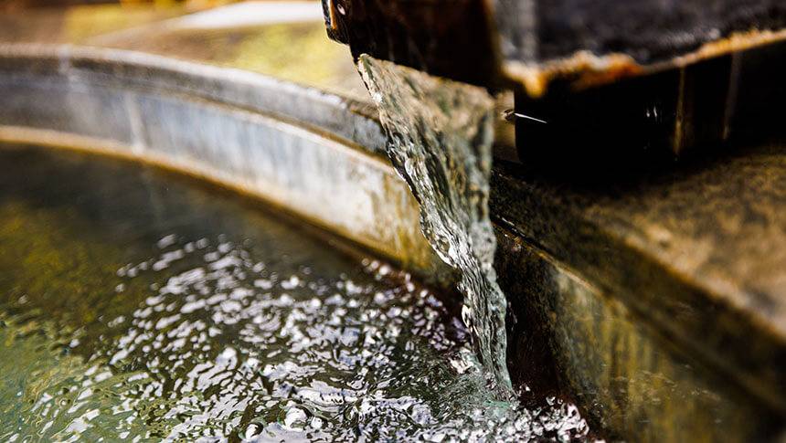 石造りの湯口から勢いよく注がれる温泉の水面。波紋が広がる様子が涼やかで、お湯の新鮮さを感じさせる。