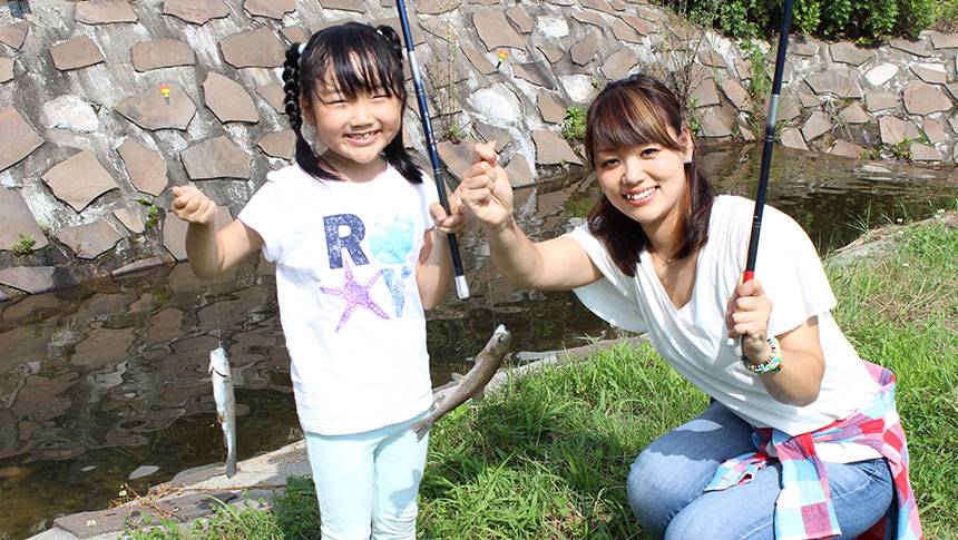 山形県の愛犬と泊まれる温泉宿「釣り宿 長者屋敷」｜屋外池で魚釣りを楽しむ親子。釣った魚を手に笑顔を見せるファミリー旅行の様子
