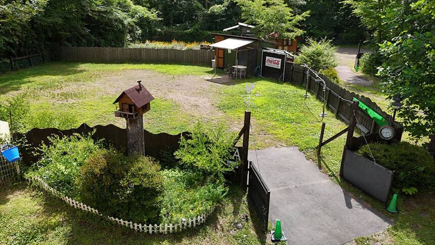 群馬県・北軽井沢の犬と泊まれる宿「ミリーズラブ」｜高い位置から撮影した、フェンスで完全に囲われた広い芝生のドッグラン。敷地内には小さな小屋のオブジェや、洗い場、休憩スペースが完備されているオートキャンプサイト