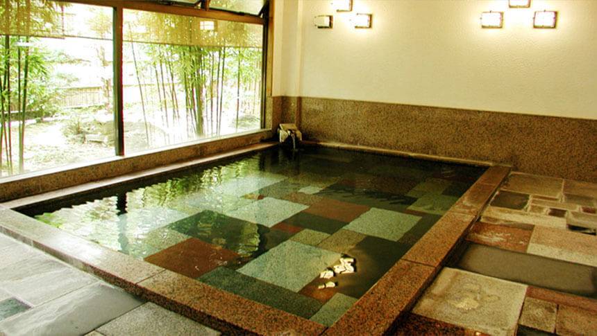 静岡県・河津温泉にある犬と泊まれる宿「河津　花小町」｜広々とした屋内大浴場。色とりどりの石が敷き詰められた浴槽があり、大きな窓からは外の竹林を眺めながら入浴できる。