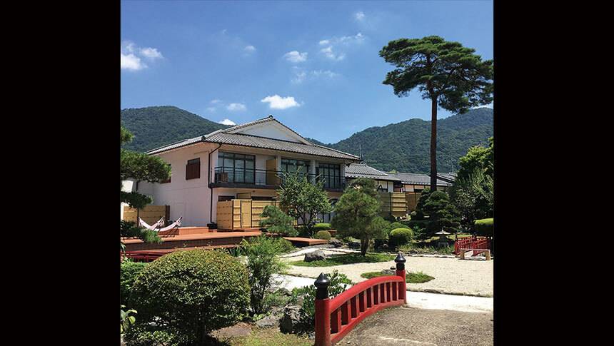 栃木県・鬼怒川にある愛犬と泊まれる温泉宿「鬼怒川絆」の美しい日本庭園。青空の下に広がる情緒豊かな庭園と、赤い橋、客室の外観