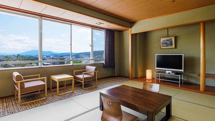 畳のスペースとリビングコーナーがある和モダンな客室。窓の外には生駒の山々と街並みが広がり、日本の情緒と快適さが融合した空間。