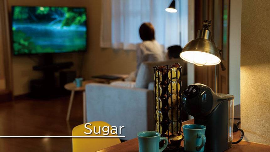 静岡県・伊豆高原の犬と泊まれる宿　ゆがふ「伊豆」｜Sugarの室内で、コーヒーマシンが置かれたカウンター越しにリビングでくつろぐカップルを映した、落ち着いた雰囲気の夜の室内風景。
